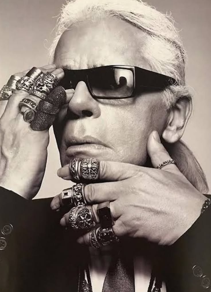 Chrome Hearts campaign portrait: a man with white hair and black sunglasses, both hands stacked with heavy silver Chrome Hearts rings, shot in black and white