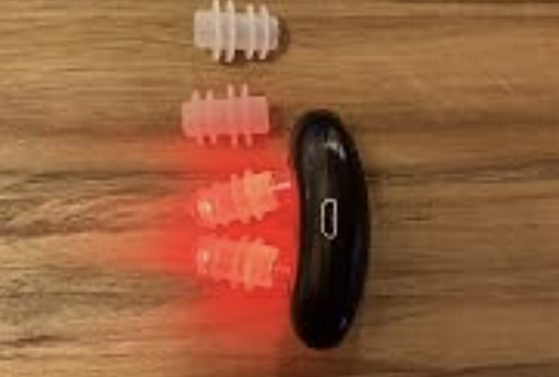 Fitora device glowing red beside its silicone nasal tips on a wooden table