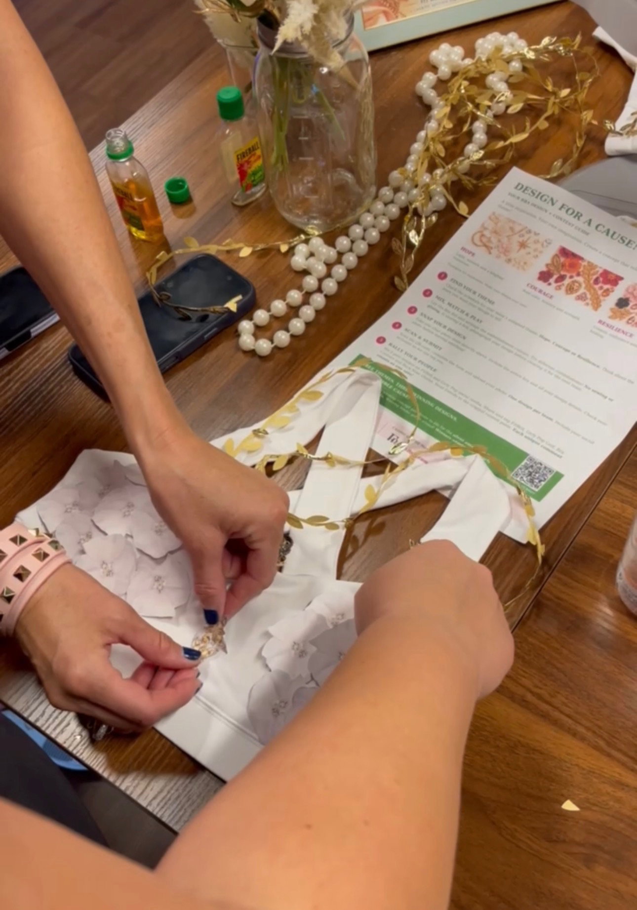 Hands decorating the white Legacy Bra with gold and white embellishments at the Golden Thread workshop