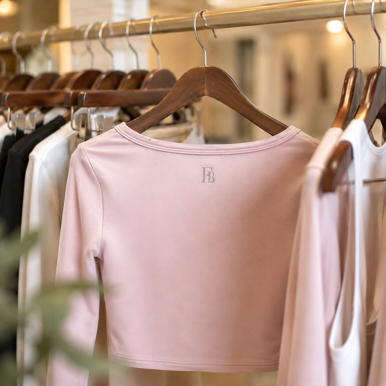 Blush pink FIT BRIT top with a scoop neckline and embroidered FB logo, hanging on a warm wooden hanger on a brass clothing rail