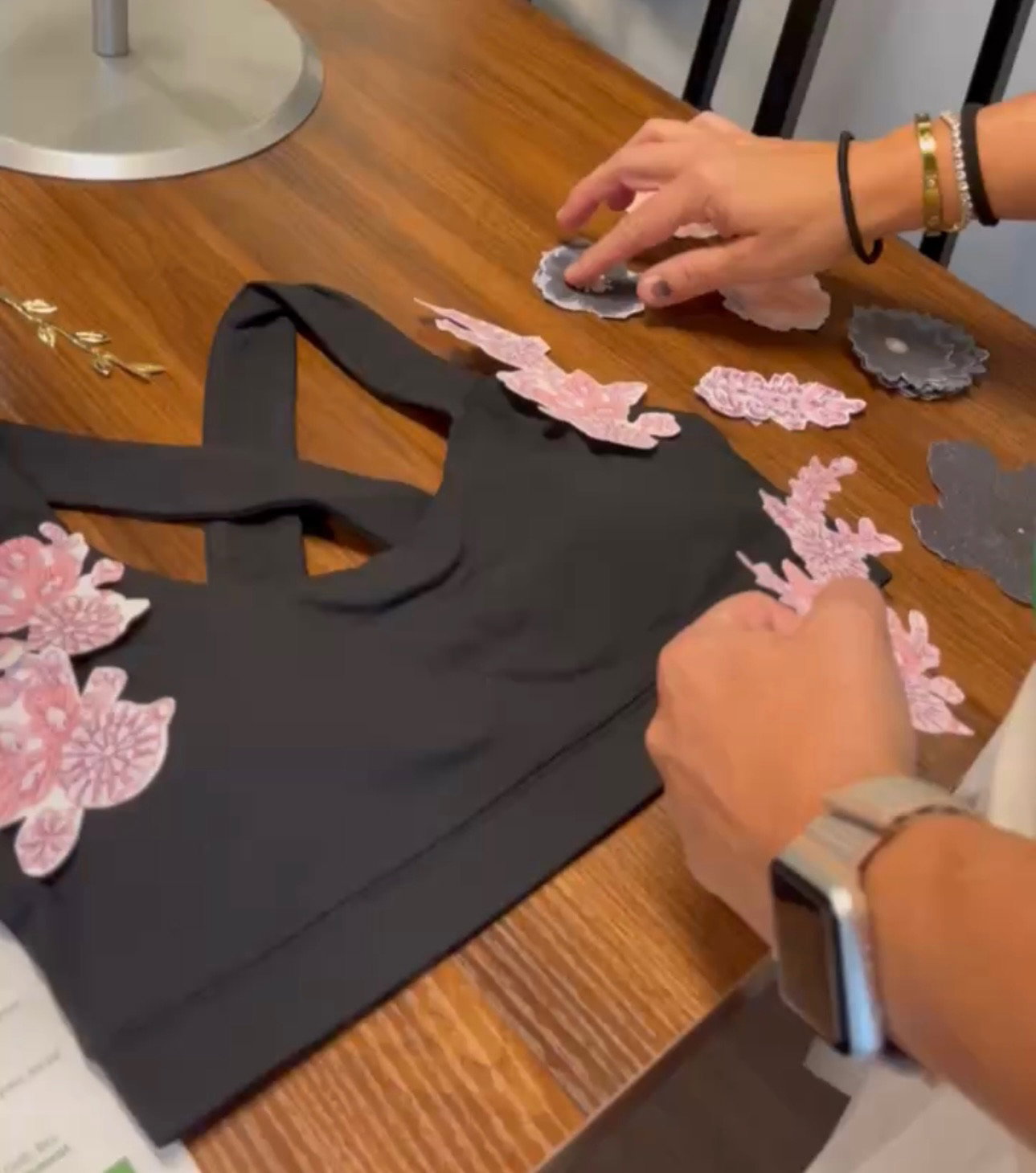 Hands arranging pink floral embellishments on the black Legacy Bra at the Golden Thread workshop