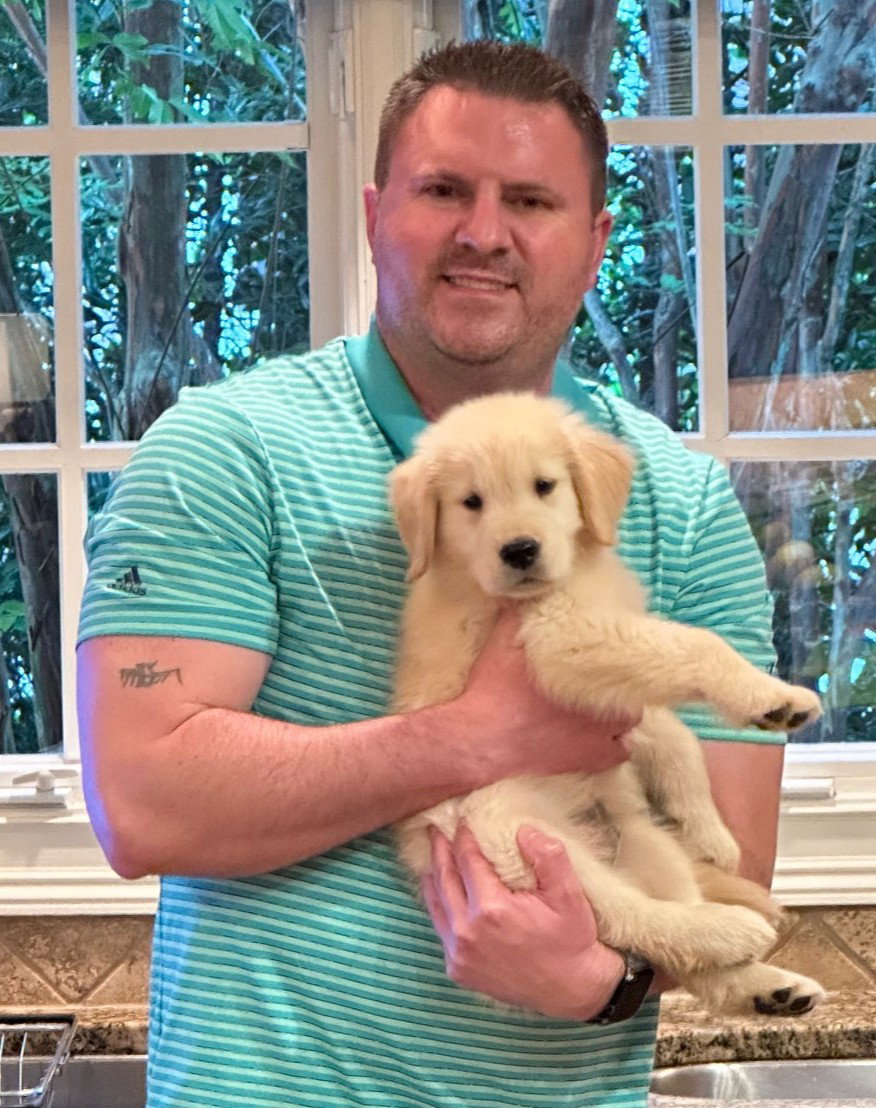 Founder Clay smiling in his kitchen while holding his golden retriever puppy, Colt
