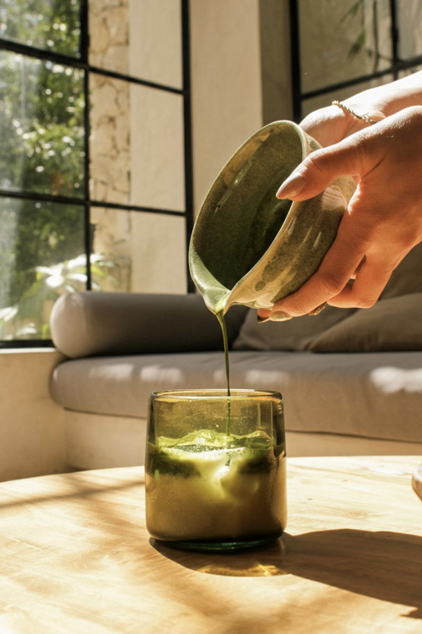 pouring matcha tea from ceramic bowl into a glass