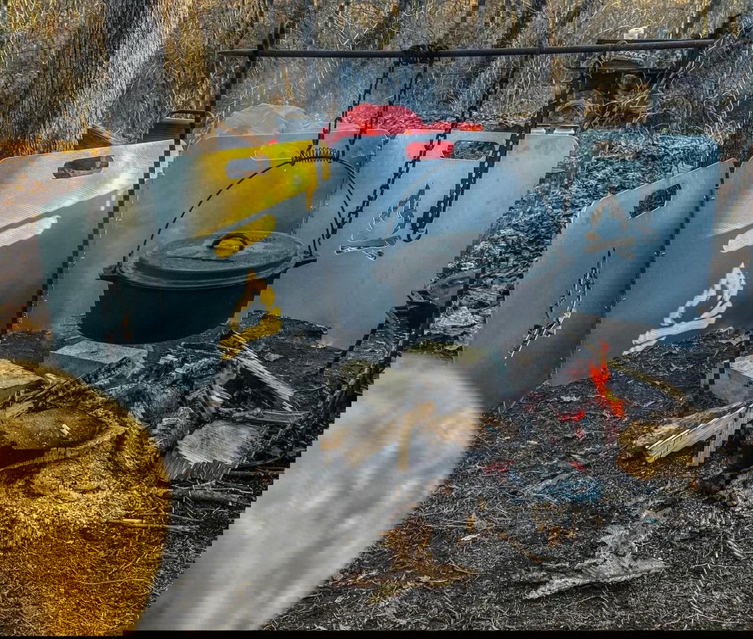 A cast iron Dutch oven hangs over a crackling campfire, surrounded by the Original Fire Reflector panels in a wooded campsite.