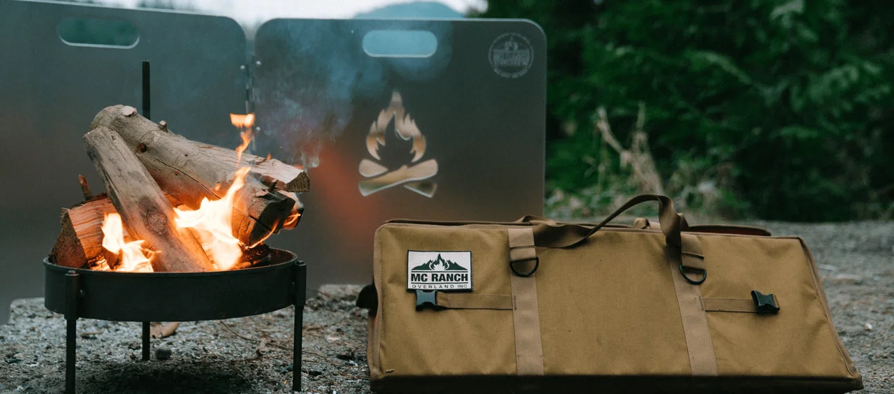 Burning campfire in a fire pit with firewood and a protective screen next to a tan carrying bag