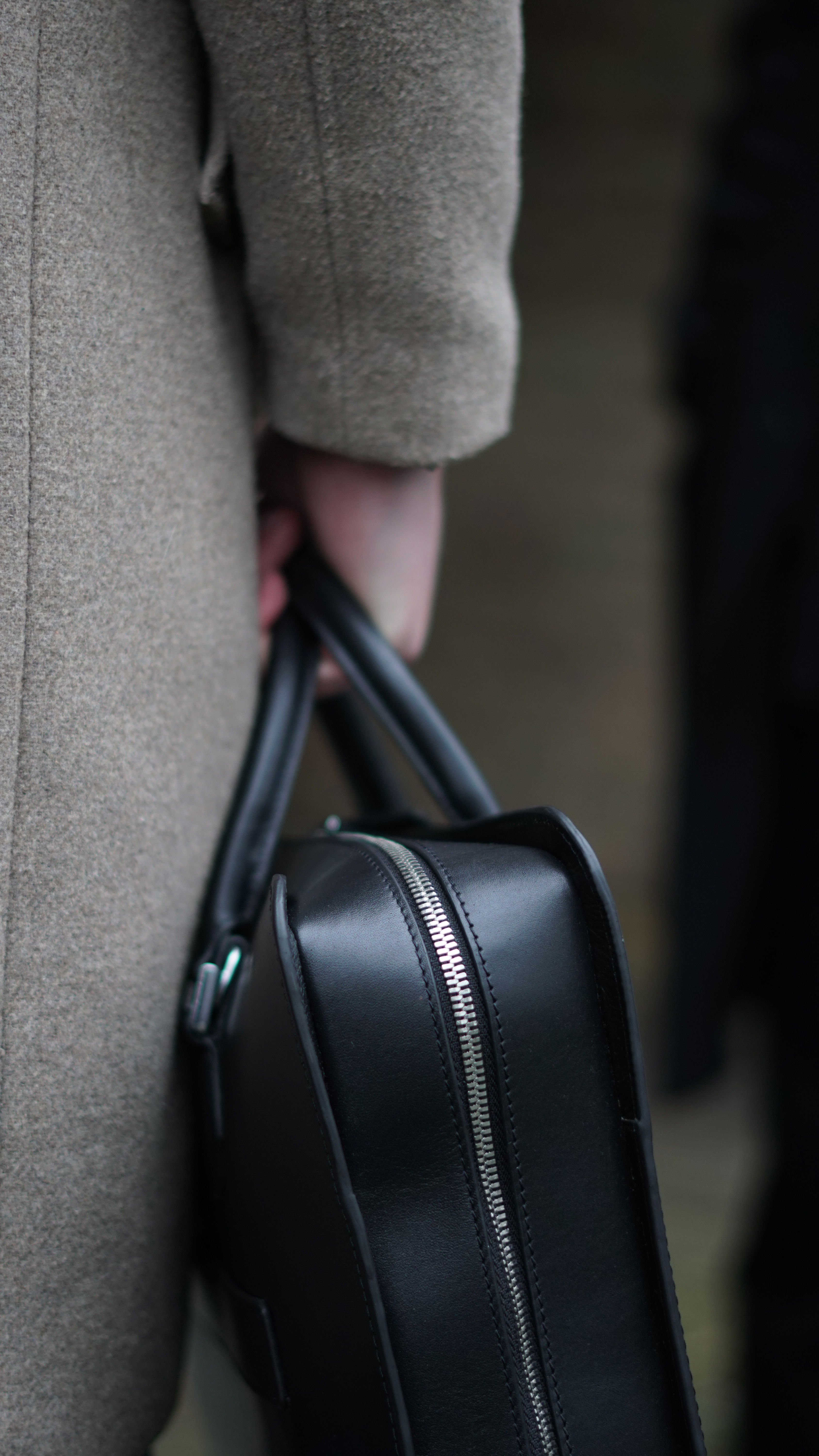 Hand carrying a black leather bag with a silver zipper