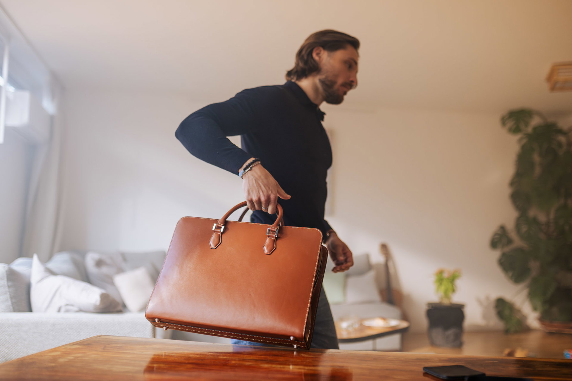 Man lifting a cognac leather Origin briefcase from a wooden table