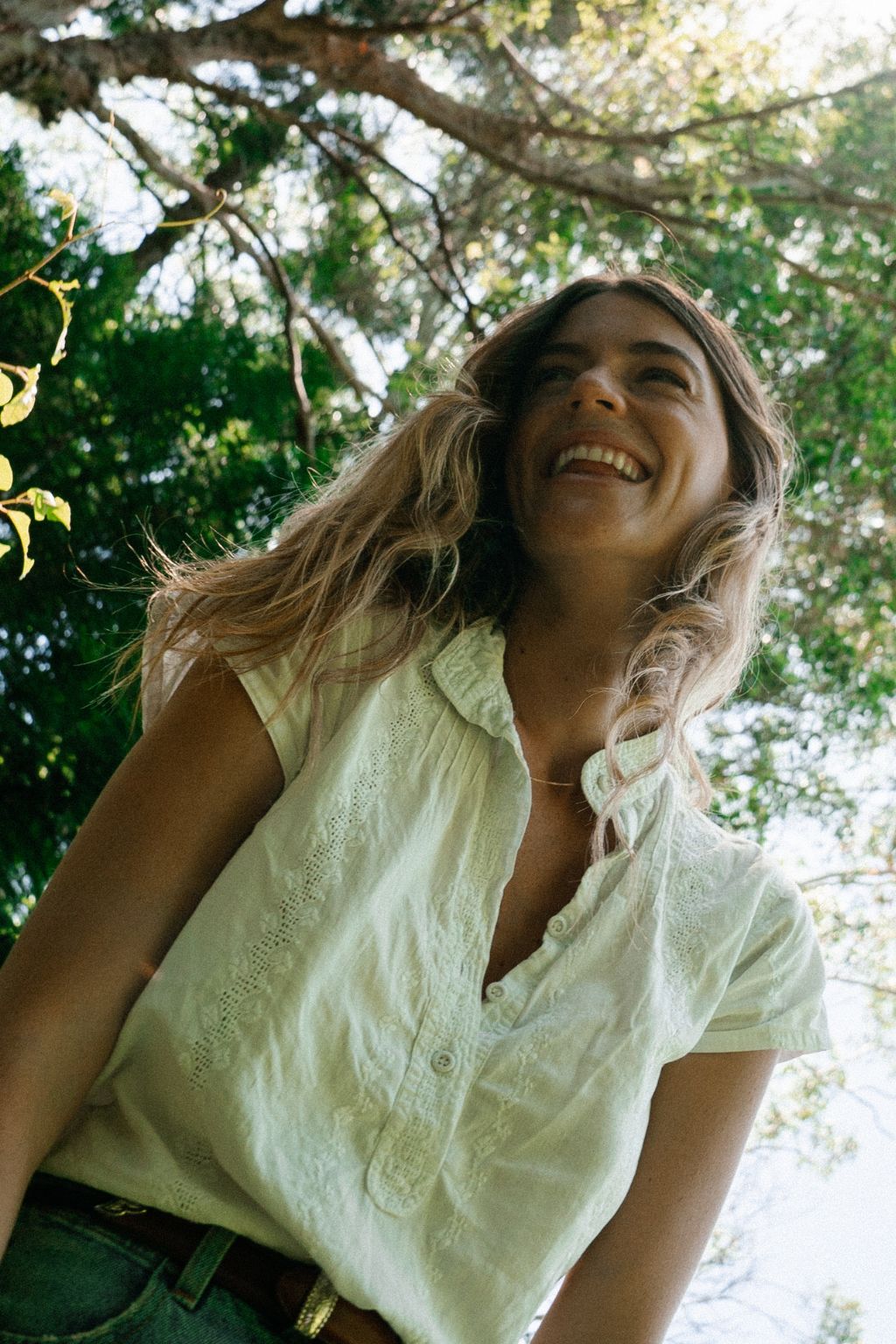 Smiling woman in a white embroidered top beneath sunlit Australian trees