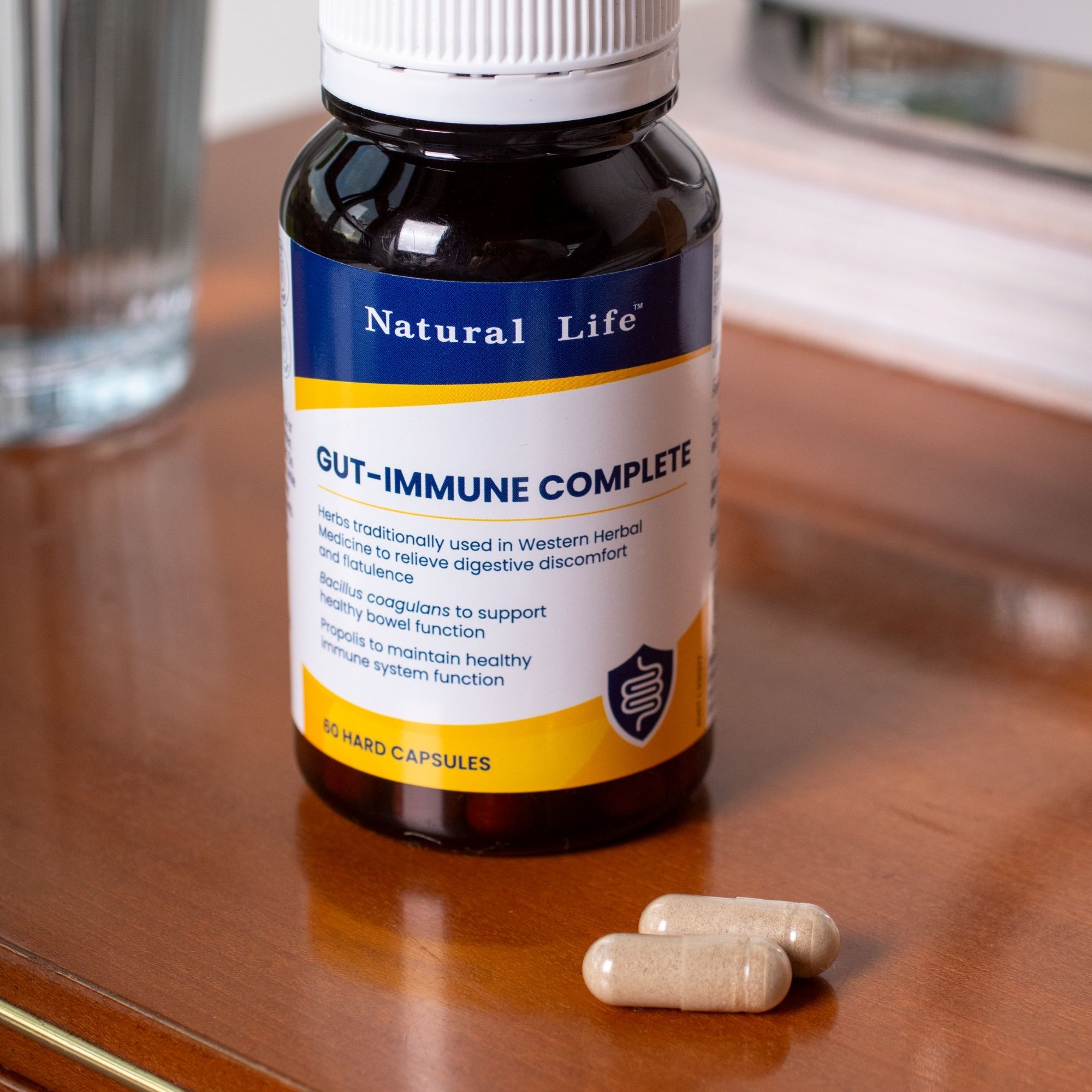 Gut-Immune Complete bottle on a cream bench beside loose capsules and laboratory glassware