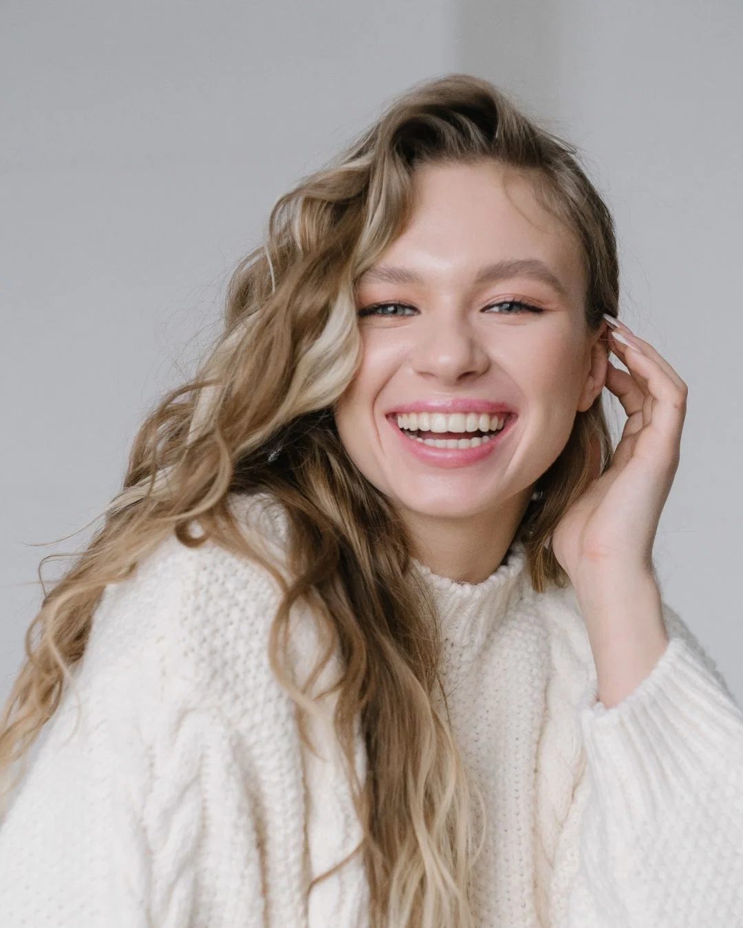 A woman in a cream knit sweater resting her hands comfortably on her stomach