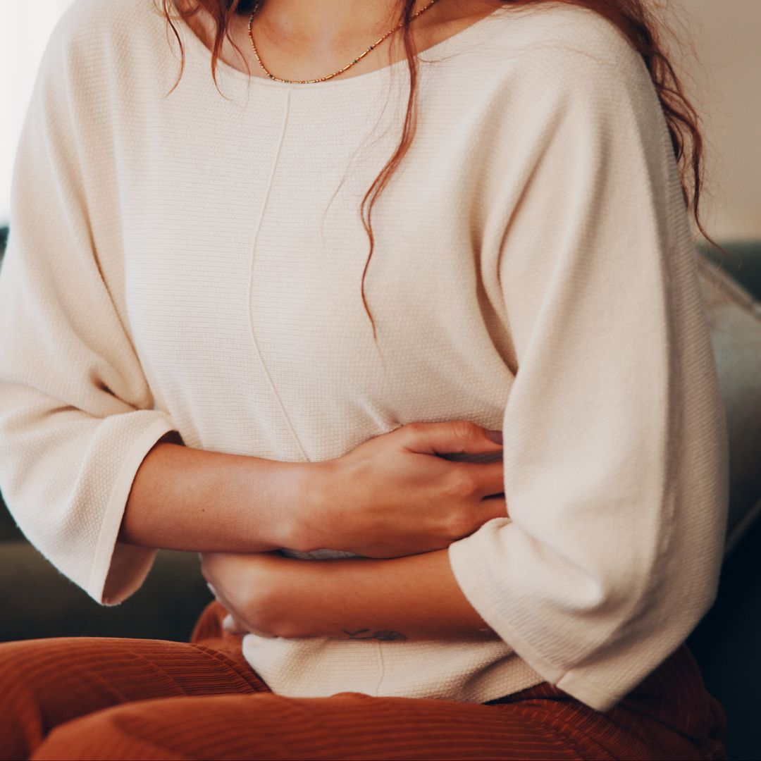 Woman sitting on a sofa holding her stomach in digestive discomfort