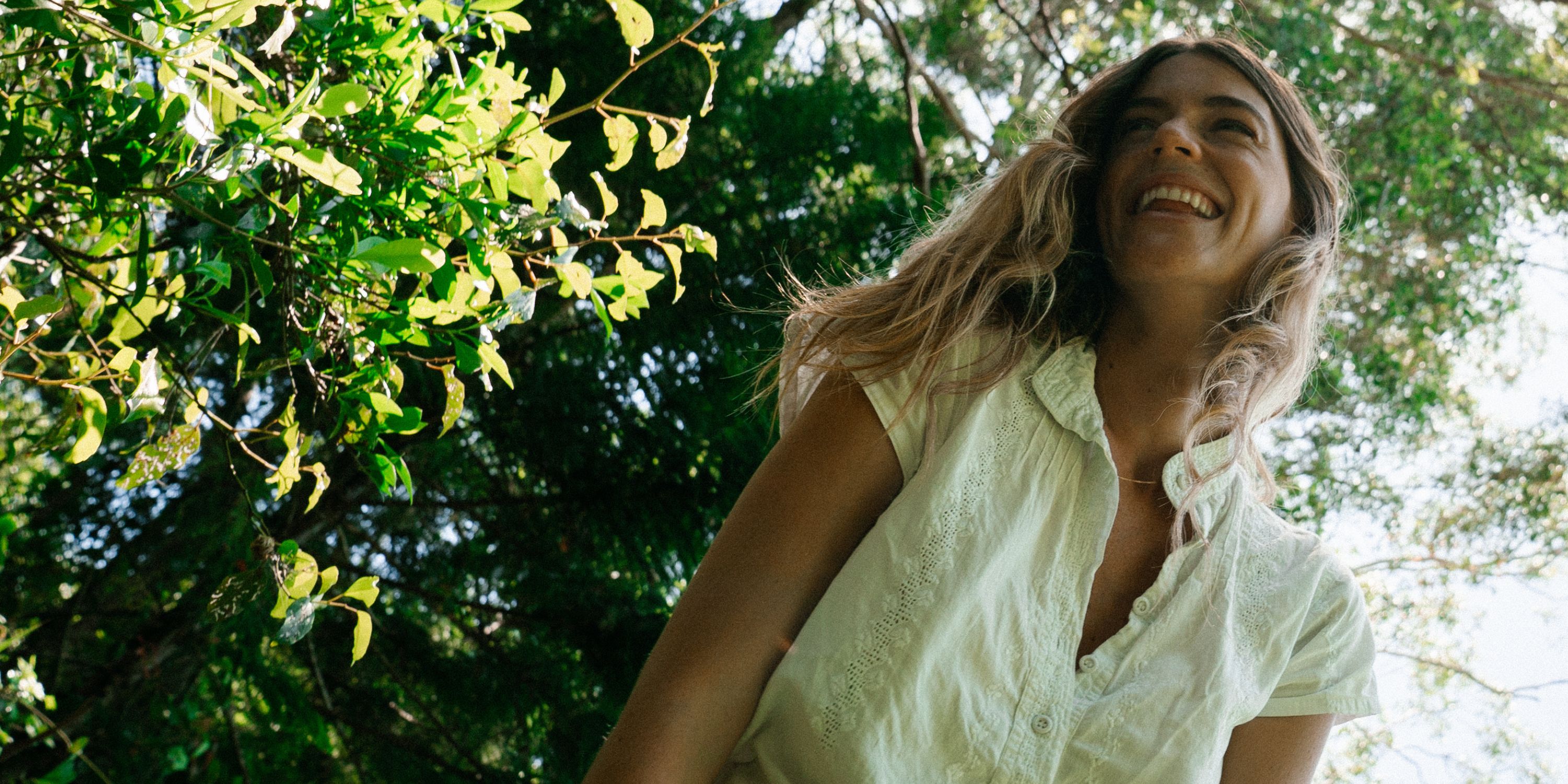 Smiling woman in a white linen top under sunlit Australian trees