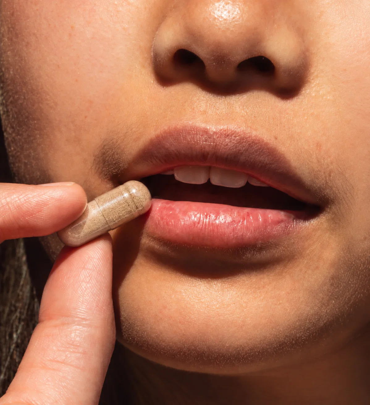 Close-up of a woman about to take a white capsule