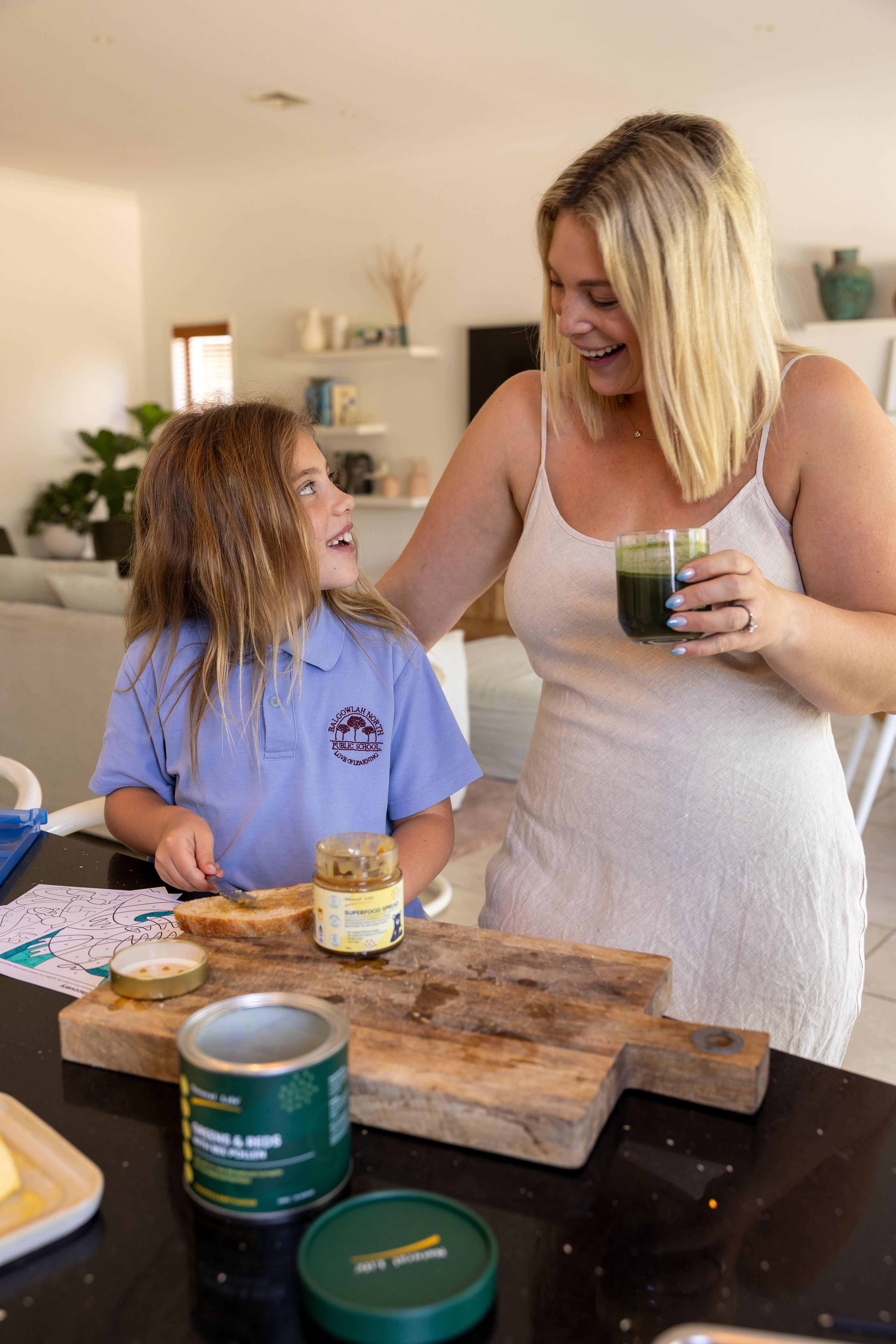 Vivid green drink being poured into a tall glass on a sunlit kitchen bench with kale and raspberries nearby