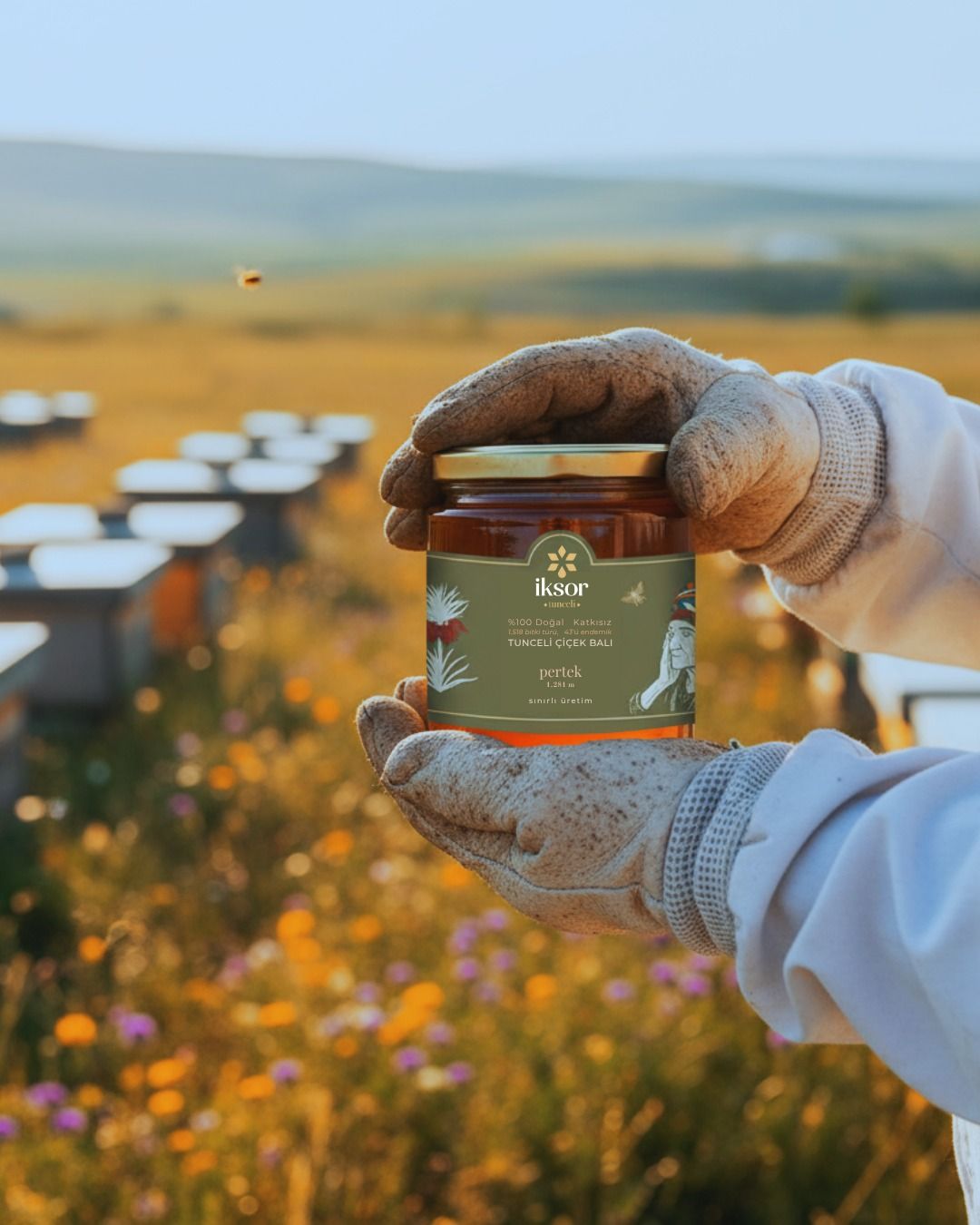 Beekeeper holding a jar of honey in a wildflower field beside hives