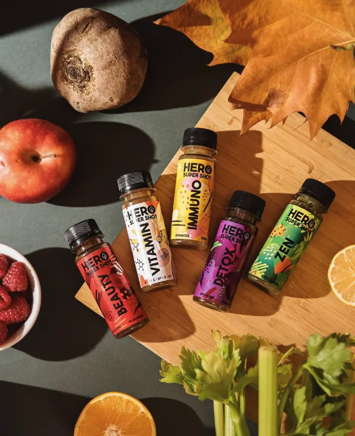 Pět HERO SuperShotů – BEAUTY, VITAMIN, IMMUNO, DETOX a ZEN – na dřevěném prkénku s řepou, jablkem, malinami a podzimním listem
