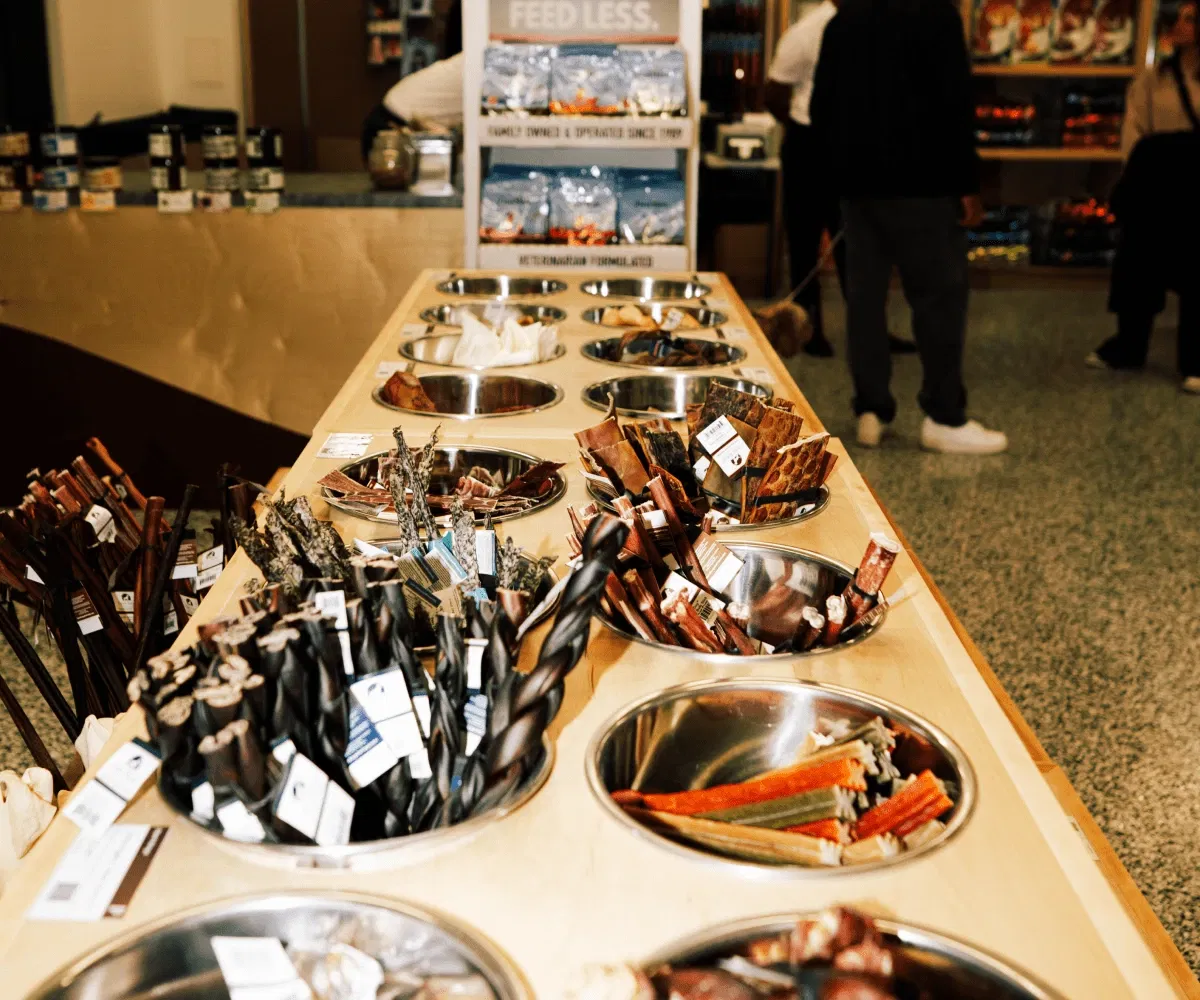 Metal bowls on wooden table filled with various pet treats in a store
