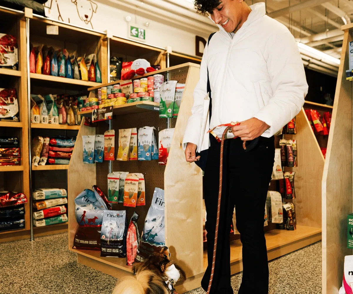 A smiling customer with their dog on a leash browsing FirstMate dog food in a Pet Planet store.