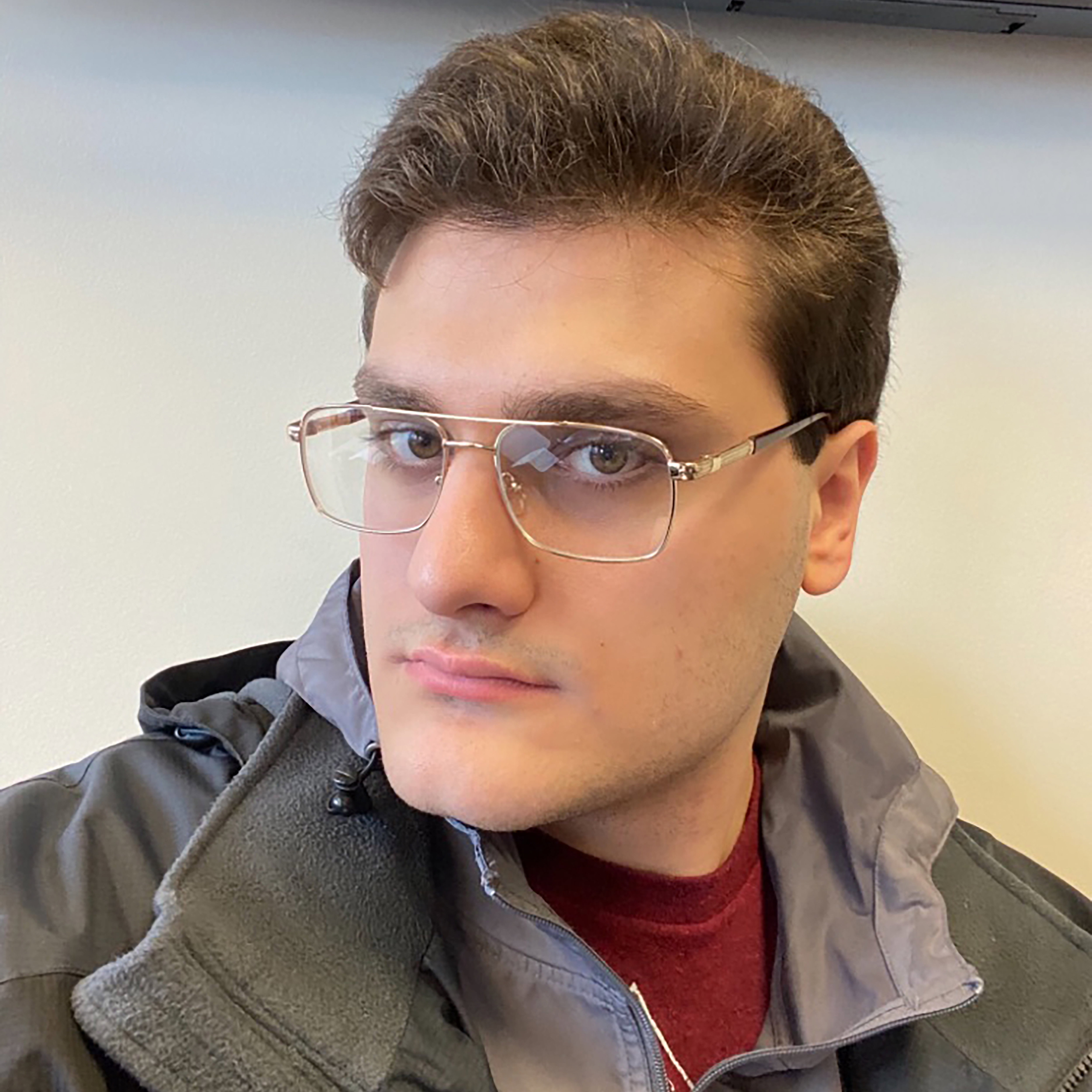 Portrait of Kristiyan-Daniel V. Iliev wearing gold-rimmed glasses and a grey jacket