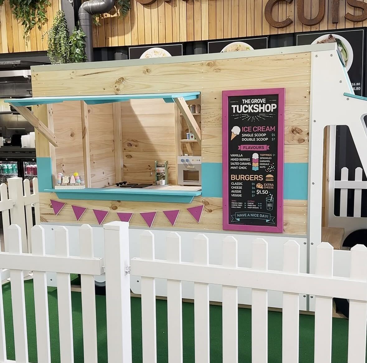 Close up of Food truck cubby house with signage showing behind a white picket fence