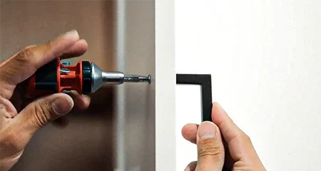 Gloved hands aligning a new white shaker drawer front on an existing oak base cabinet, with a concealed hinge on the open door and a square and level on the counter