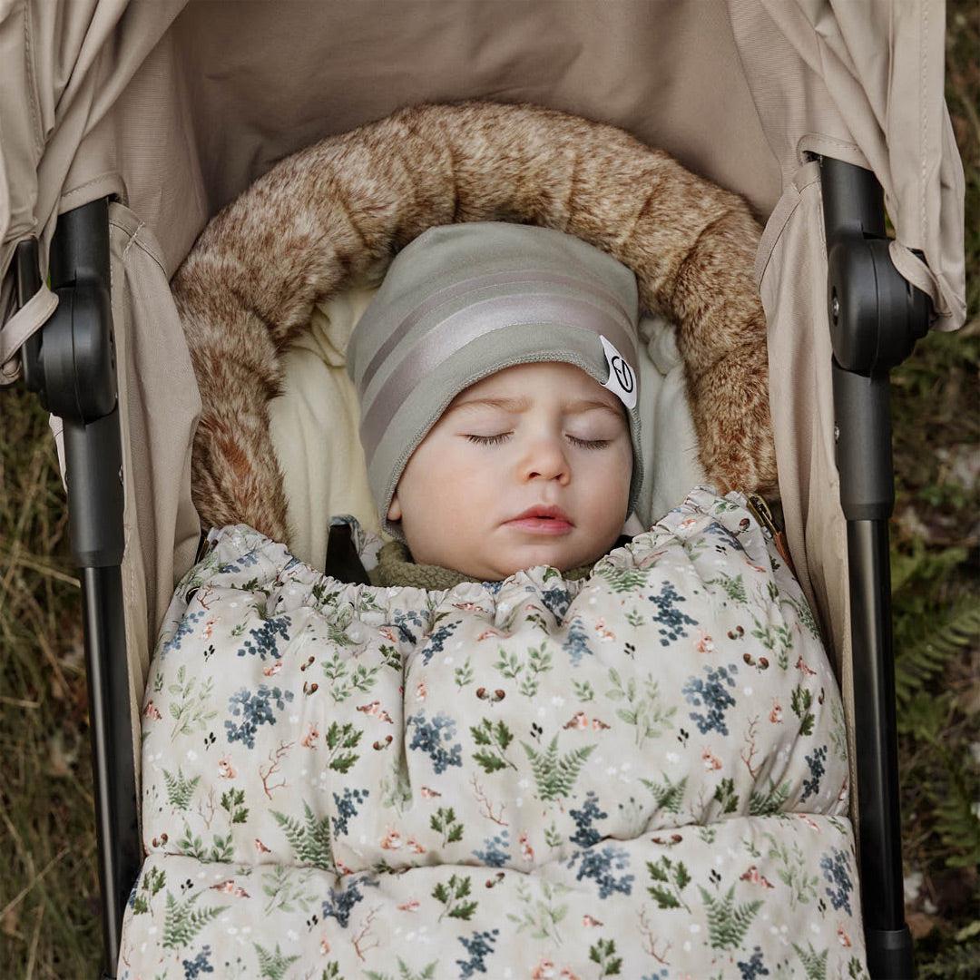 Baby asleep in a pushchair, tucked into a floral woodland-print footmuff with a faux-fur hood trim
