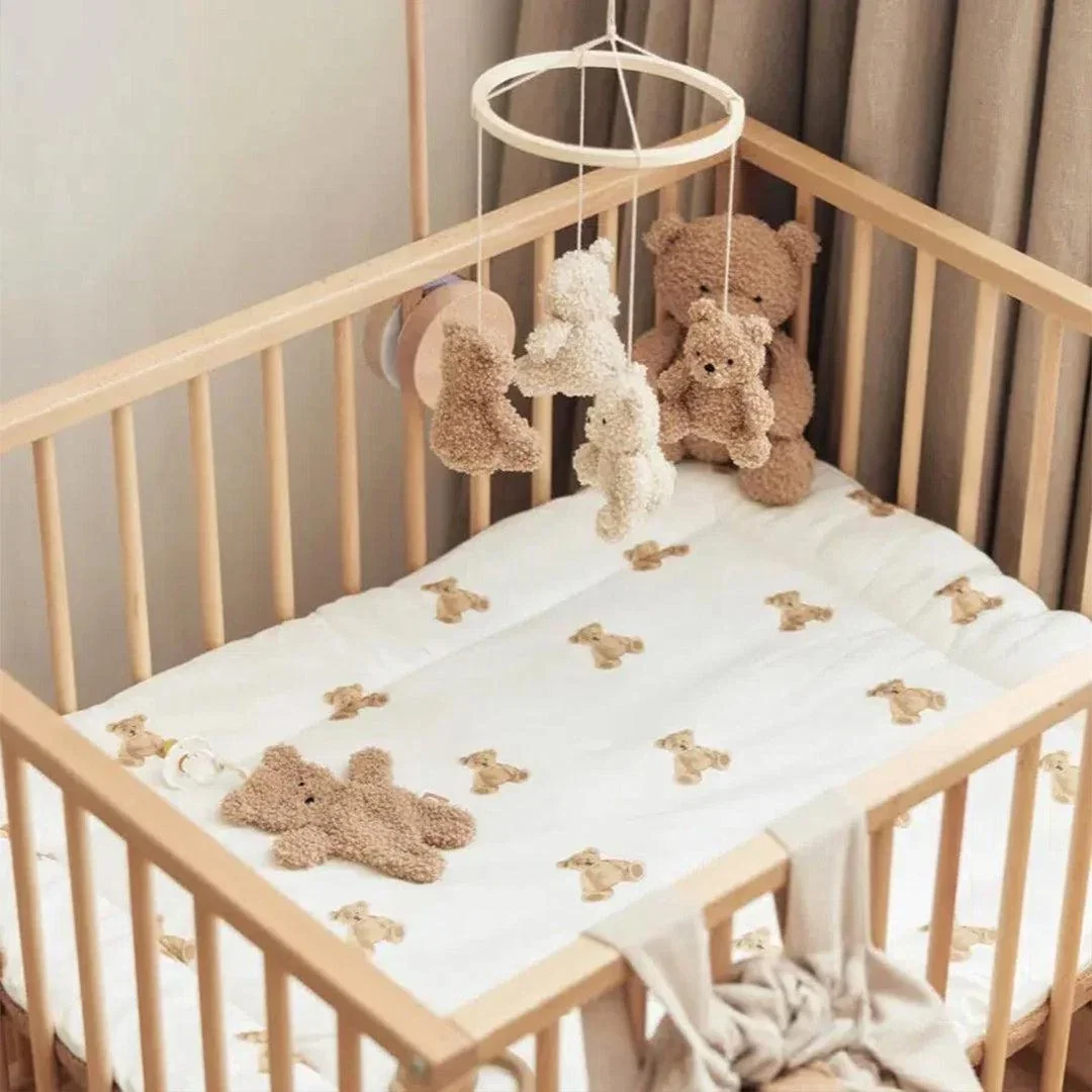 Wooden cot with a teddy bear print mattress, a hanging teddy mobile and cuddly bears in a calm neutral nursery