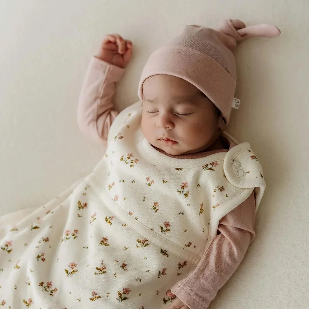 Sleeping baby in a floral sleeping bag and a pink knotted hat