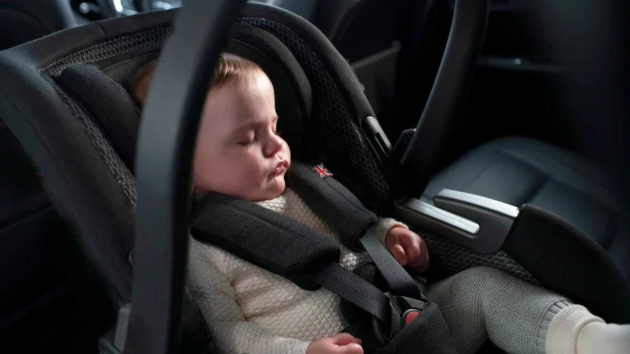 Baby in a cream knitted jumper sleeping peacefully in a black Silver Cross infant car seat in the back of a car