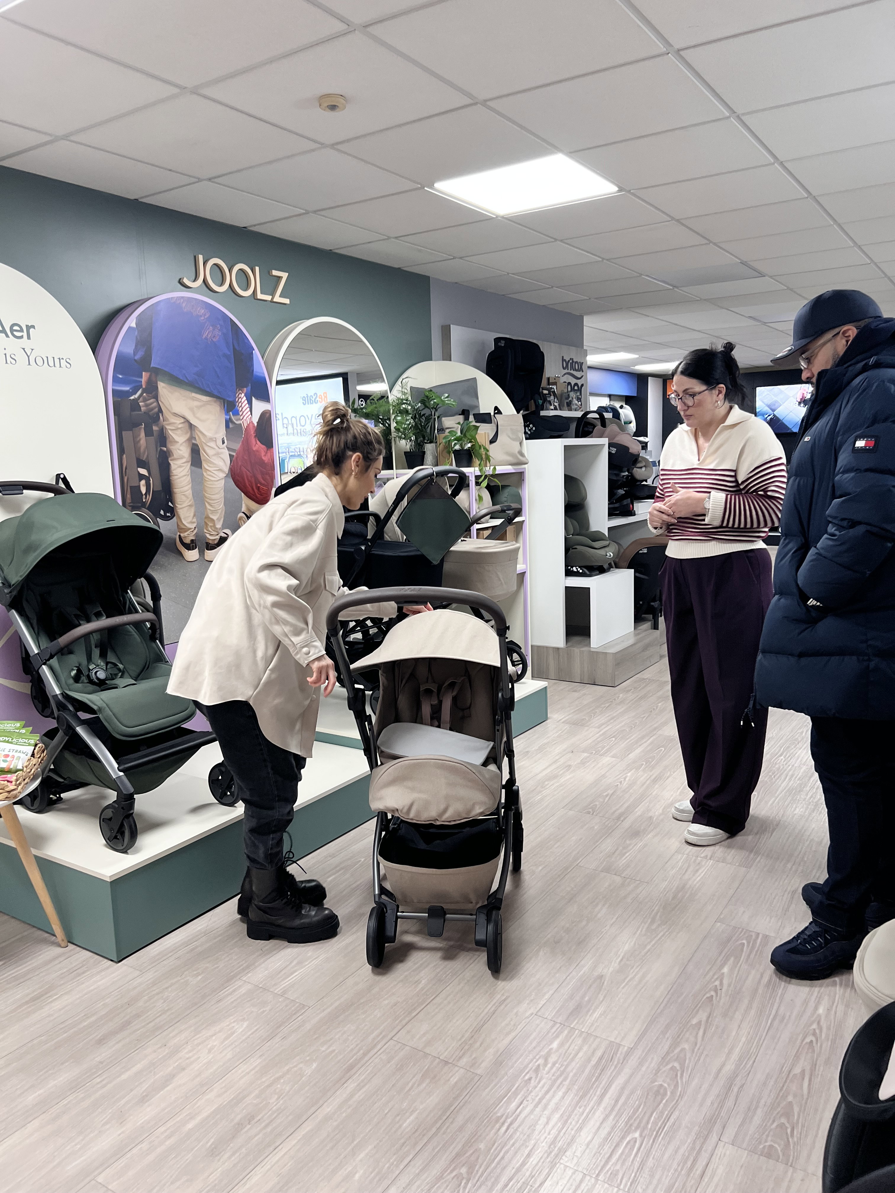 Smiling nursery expert assembling a new pushchair with a carrycot in store as a young couple looks on