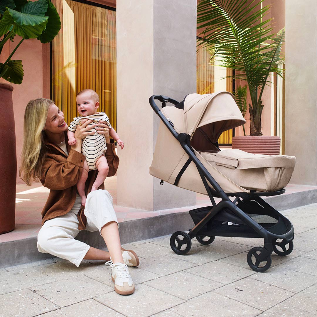 Smiling parents with their baby in a beige CYBEX Beezy stroller beside sunlit stone steps