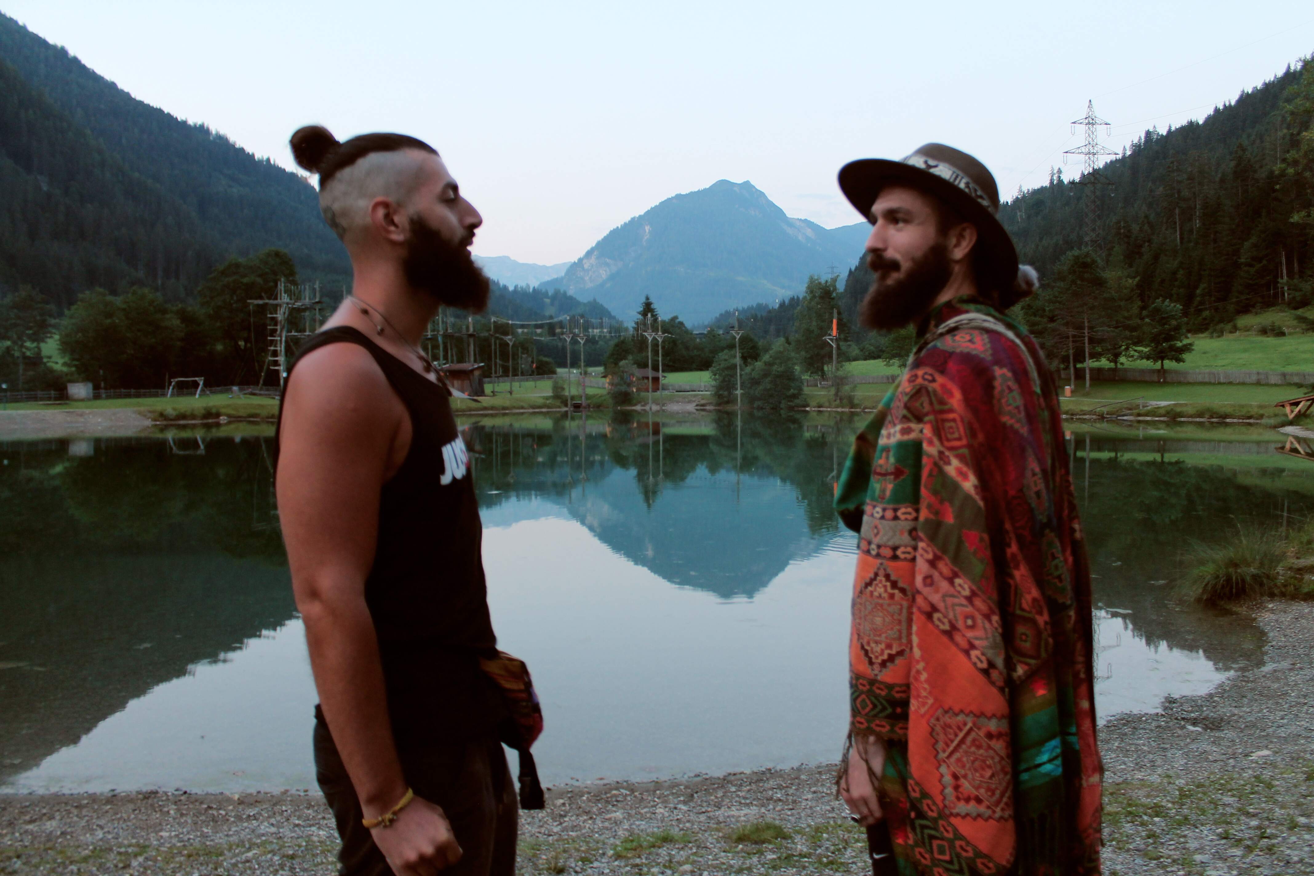 Junes Sami Bakkar and Tarek Bakkar facing each other beside a still mountain lake in the Alps