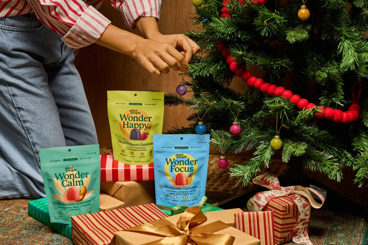 Hands hanging an ornament on a Christmas tree above Wonder Happy, Wonder Focus and Wonder Calm gummy pouches on wrapped gifts