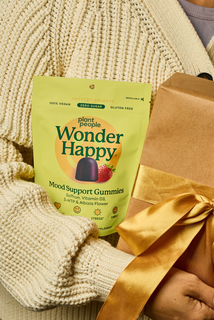 Wonder Happy Mood Support Gummies pouch on a cream knit blanket beside hot cocoa, pine and a small wrapped gift