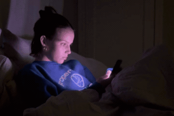 Woman lying awake in bed at night, scrolling on her phone