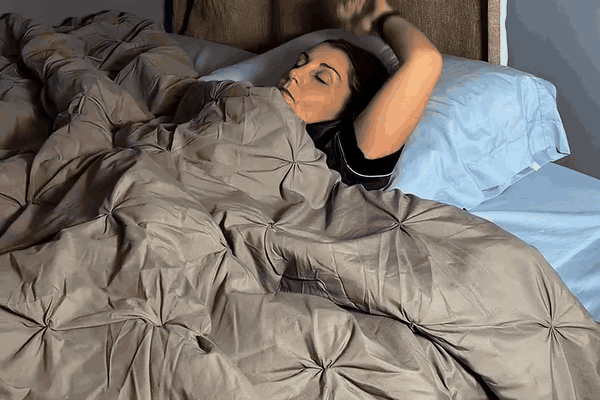 Midlife woman sitting on the edge of her bed in the morning, rubbing her temple and looking groggy