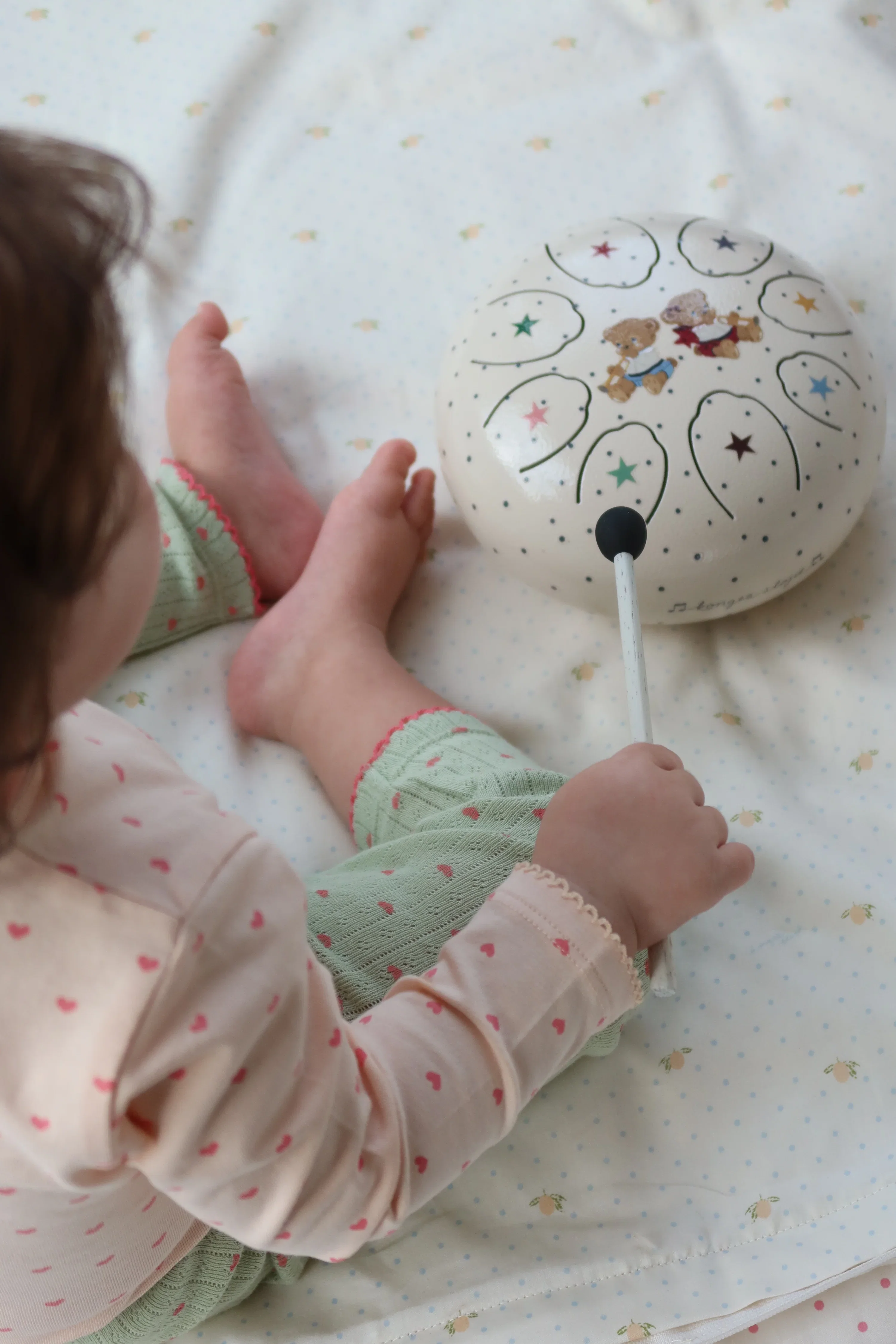 A laughing baby shaking a wooden maraca while a grown-up holds a small frame drum