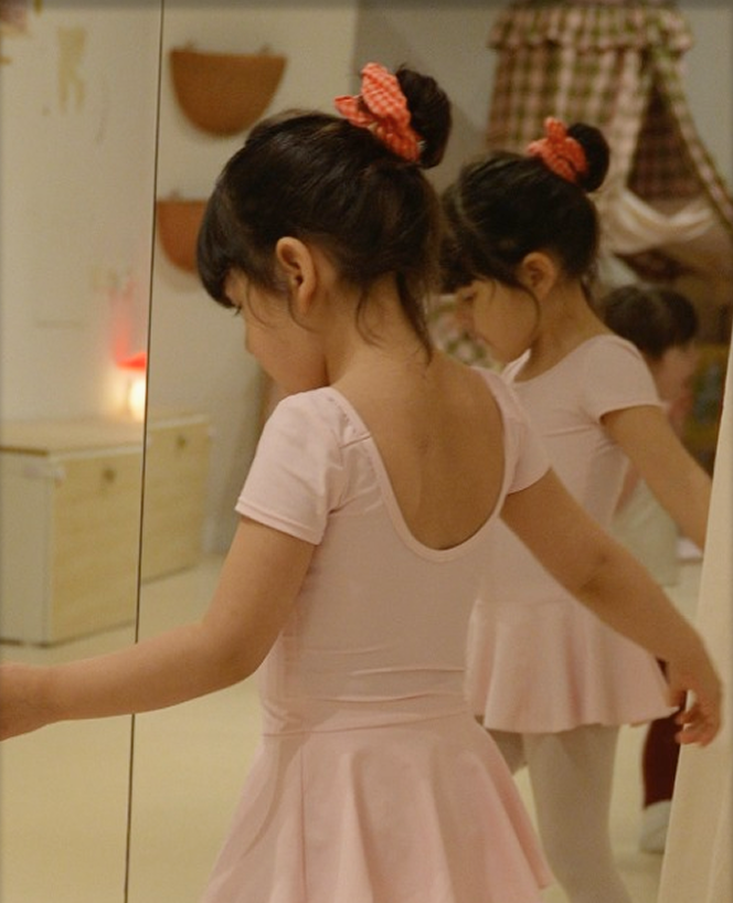 Little girls in pink leotards and gingham scrunchies practising ballet at the mirror