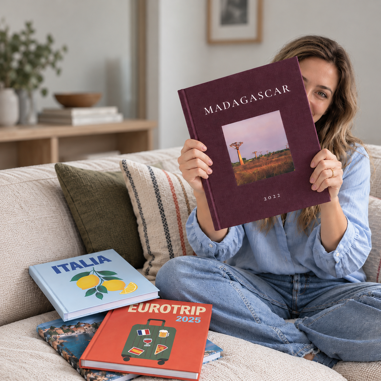 Mujer en un sofá sosteniendo su fotolibro Pictoset de Madagascar, junto a otros álbumes de viaje