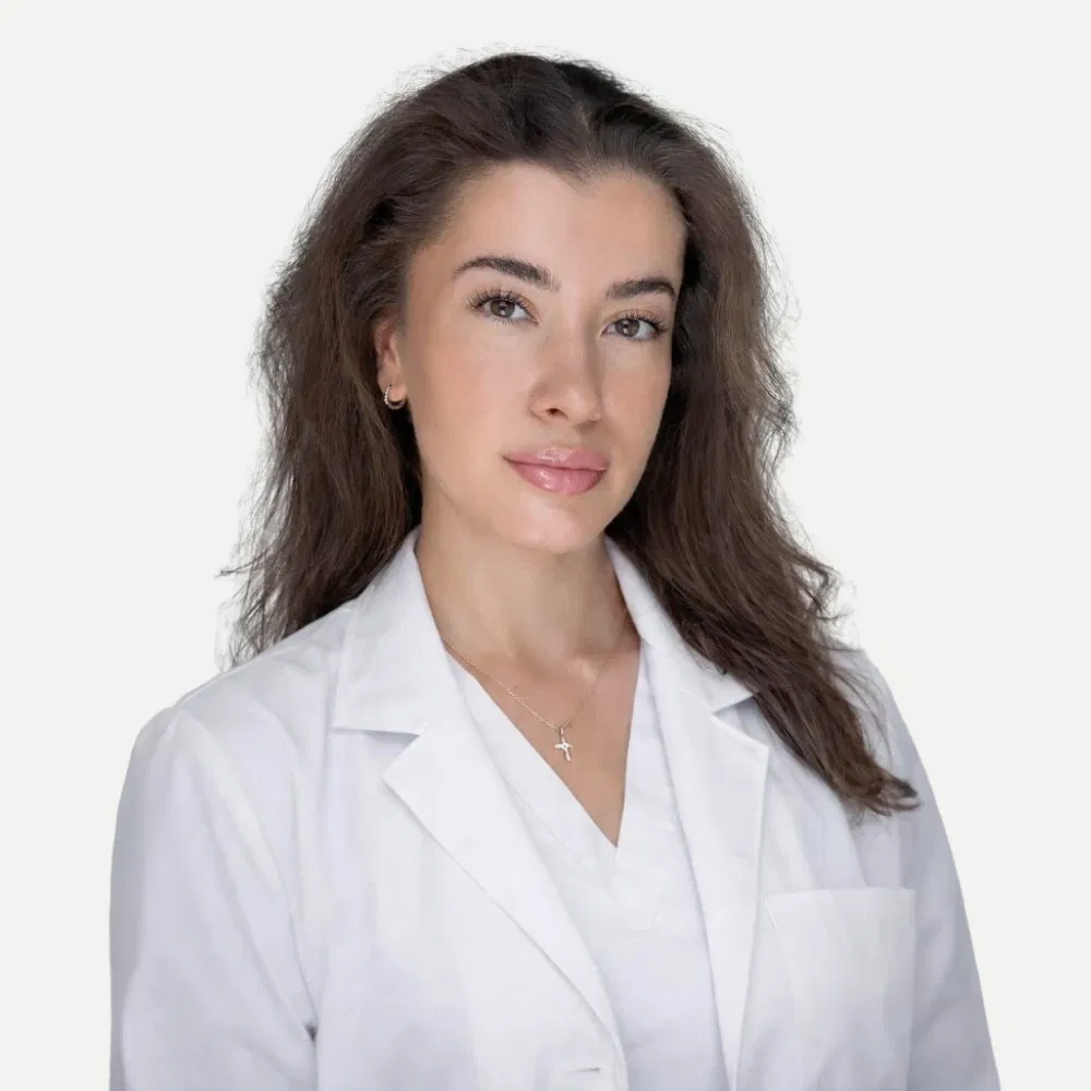 Portrait of a woman with brown hair wearing a white medical coat and a cross necklace