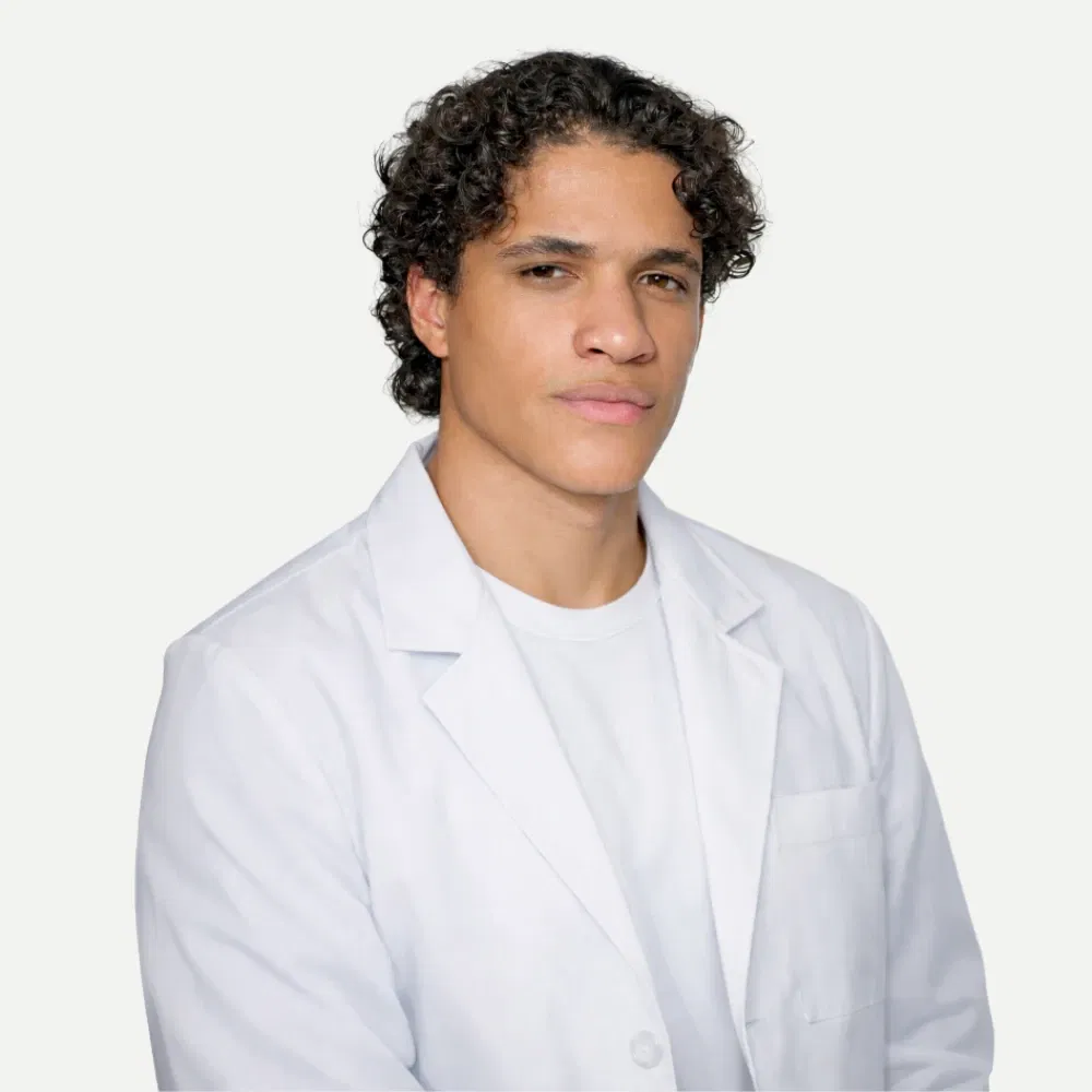 Portrait of a young man with curly hair wearing a white lab coat and white shirt