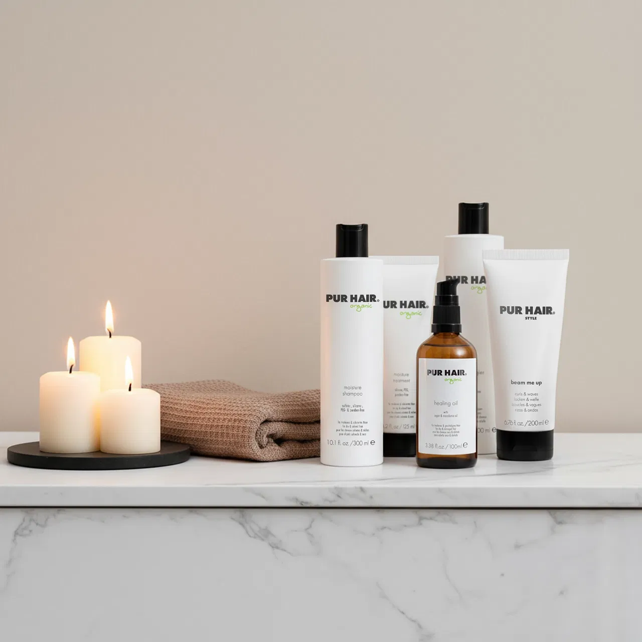 Kerzen, gefaltetes Handtuch und PUR HAIR Haarpflegeprodukte auf Marmorfläche.