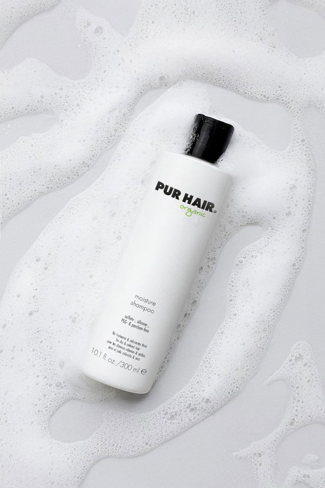 Weiße Flasche mit PUR HAIR Organic Feuchtigkeitsshampoo auf einer schaumigen Oberfläche mit Blasen.