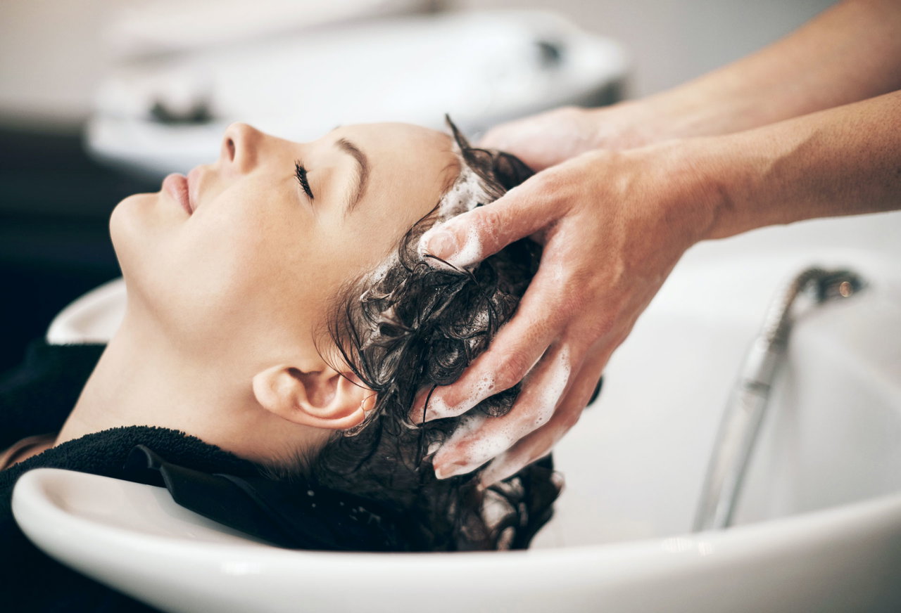 Frau, die mit geschlossenen Augen entspannt, während ihr im Friseursalon die Haare gewaschen werden.