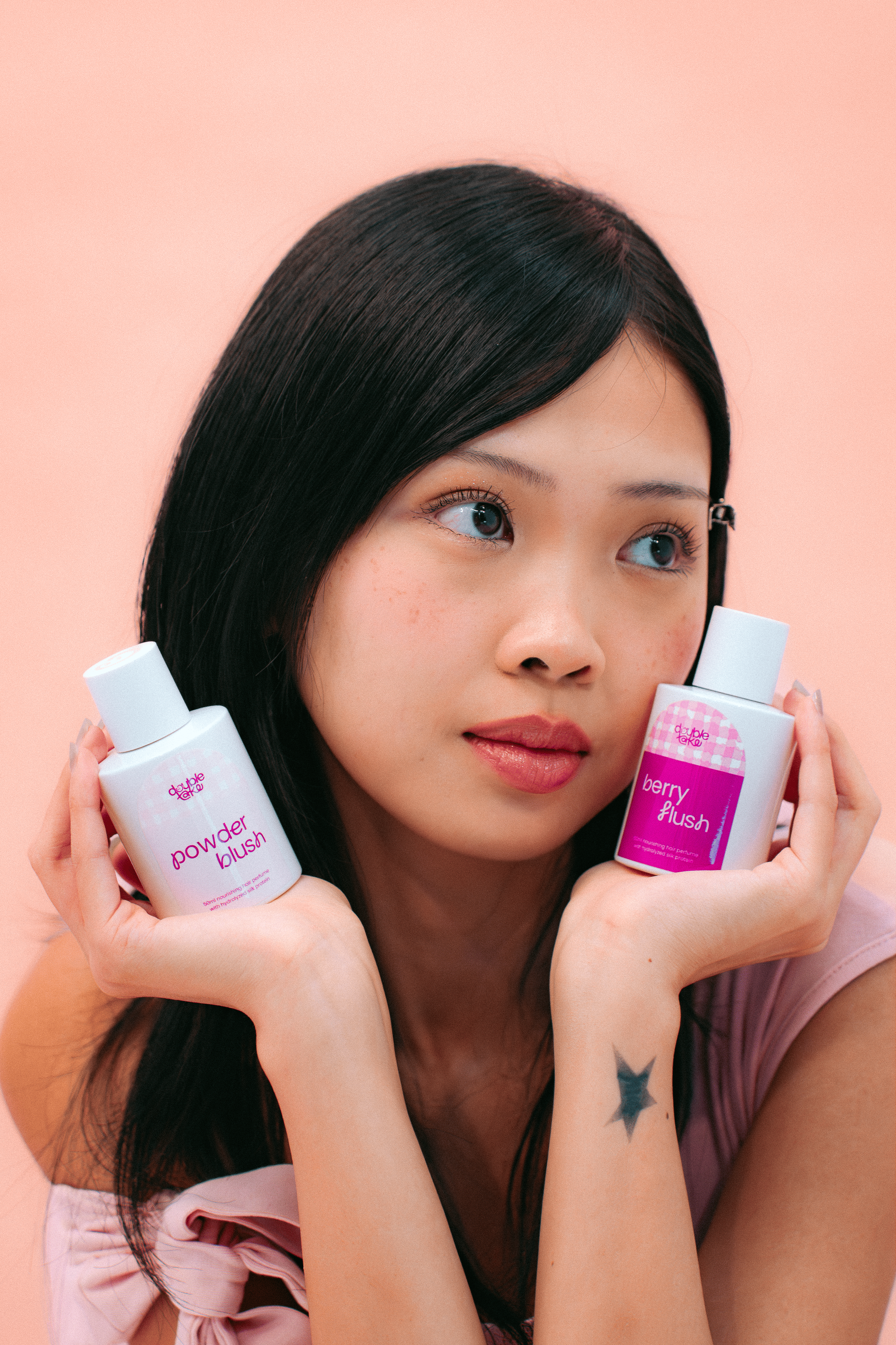 Woman holding Powder Blush and Berry Flush hair perfumes beside her face