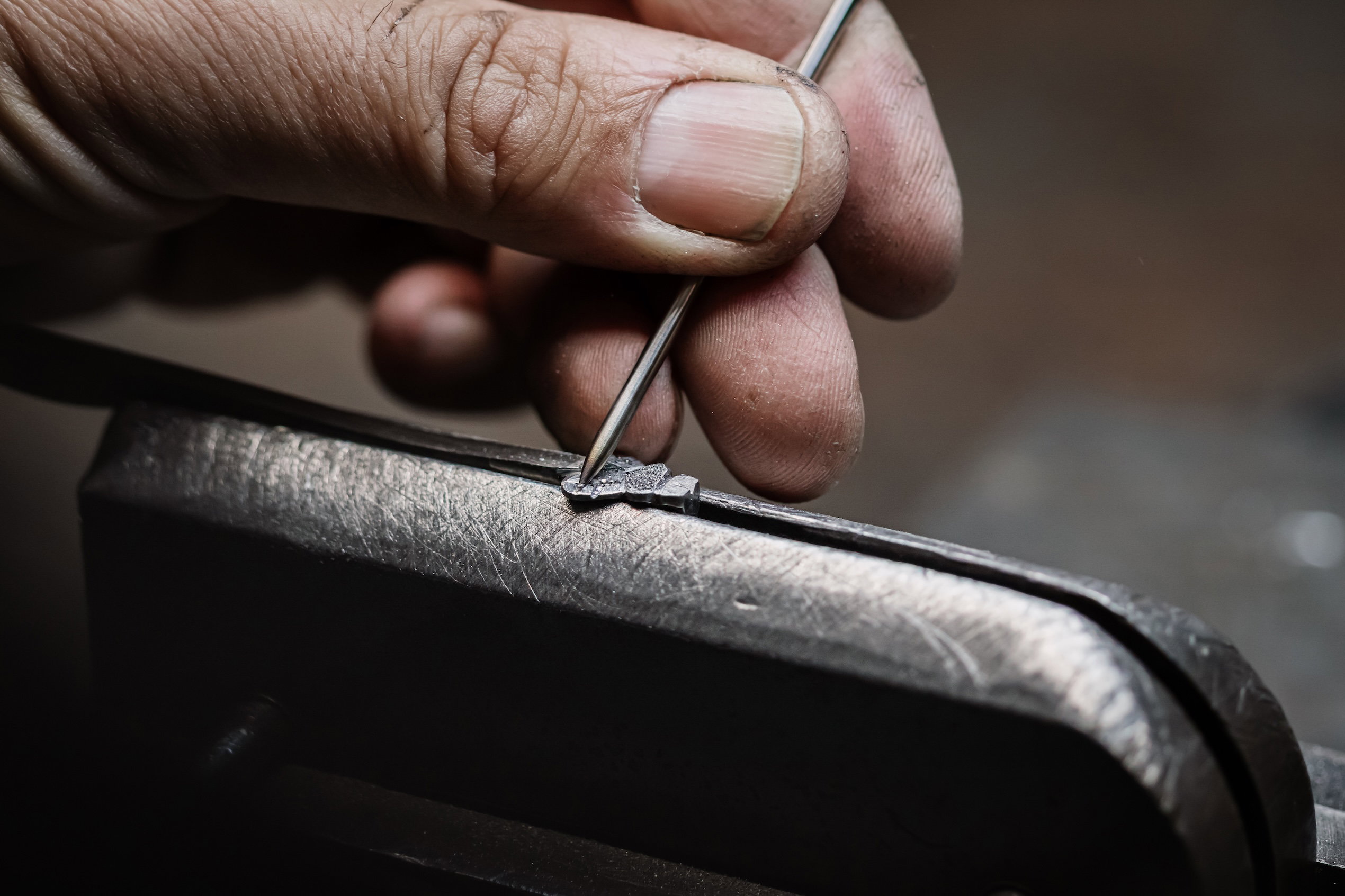 A cutler's hand chiselling the signature bee of a Laguiole knife by hand with a fine steel tool in the Forge de Laguiole workshop