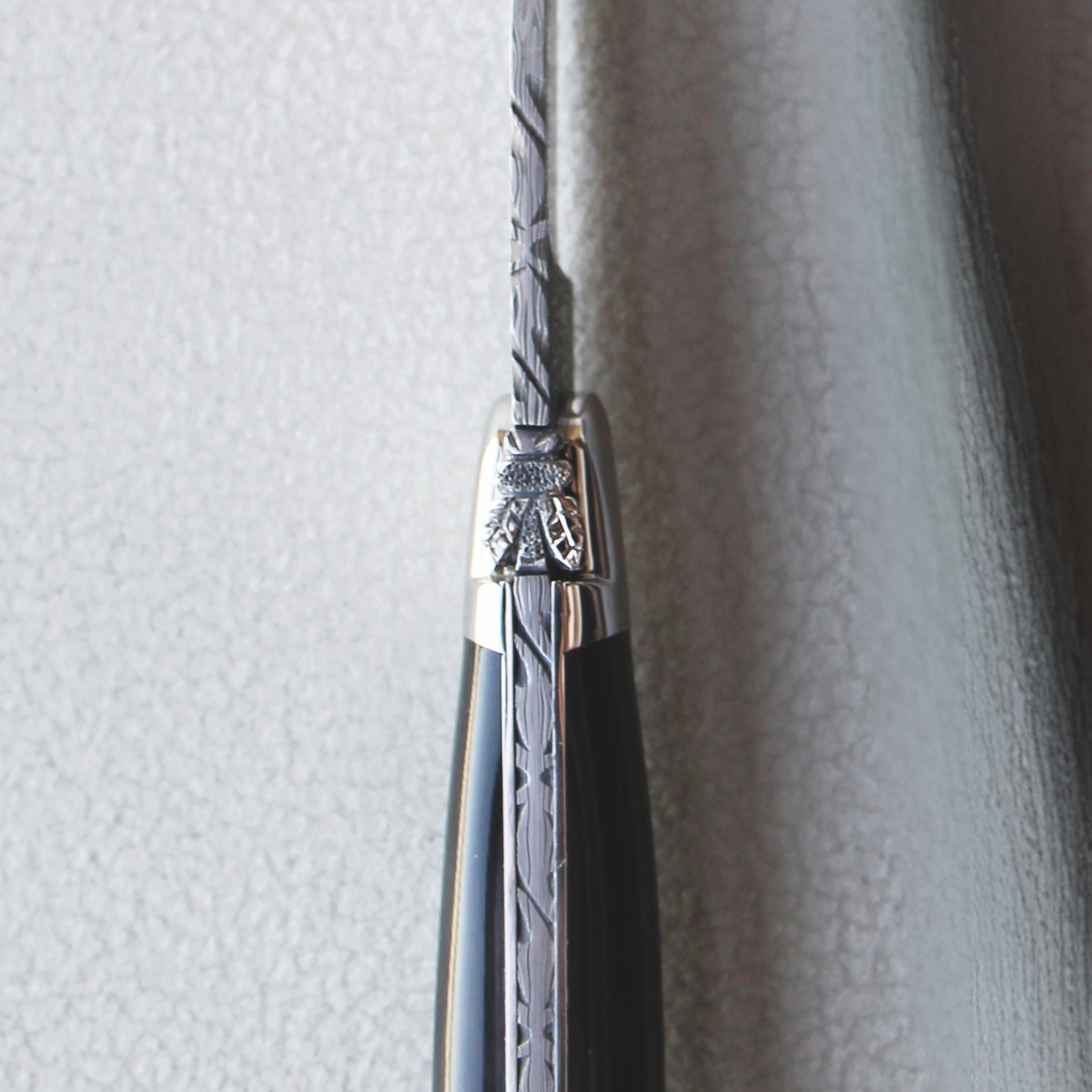 Macro close-up of the hand-chiselled bee and spring on the spine of a Collection Range dark horn Laguiole table knife with Damascus steel blade
