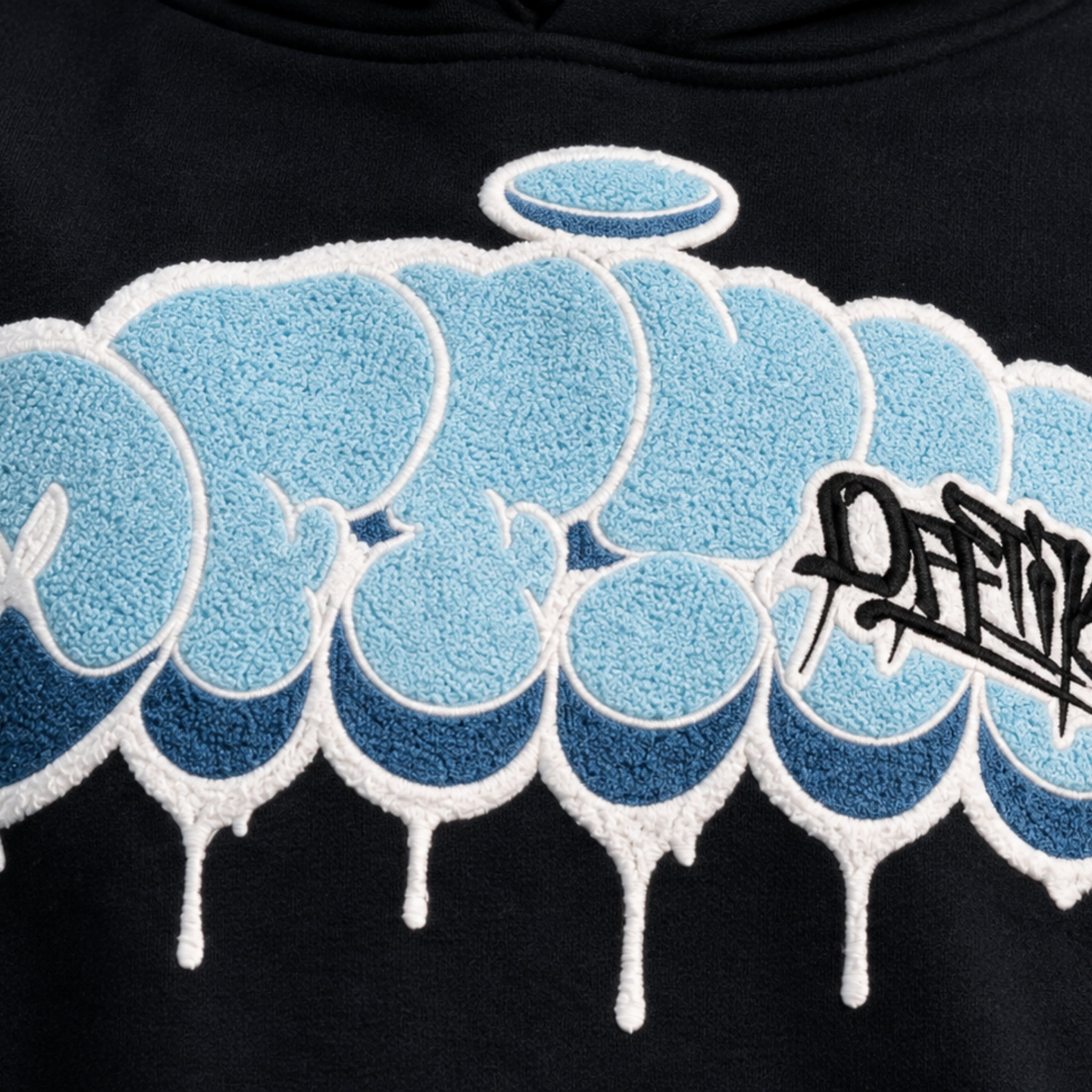 Close-up of the Throwy's blue and white bubble chenille drip lettering with halo and black OFFTIK tag script on black fleece
