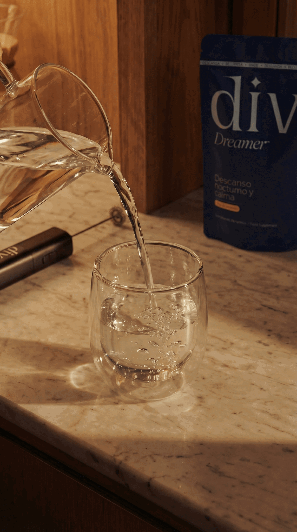Agua vertiéndose en un vaso de cristal sobre una encimera de mármol con luz cálida de tarde