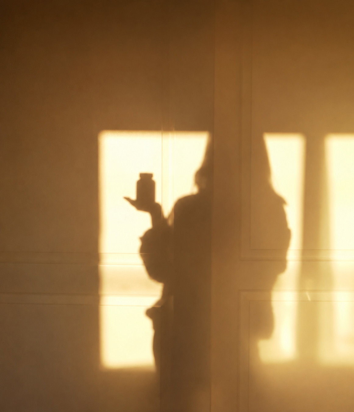 A silhouette holding up a bottle of RESET™ in warm morning sunlight